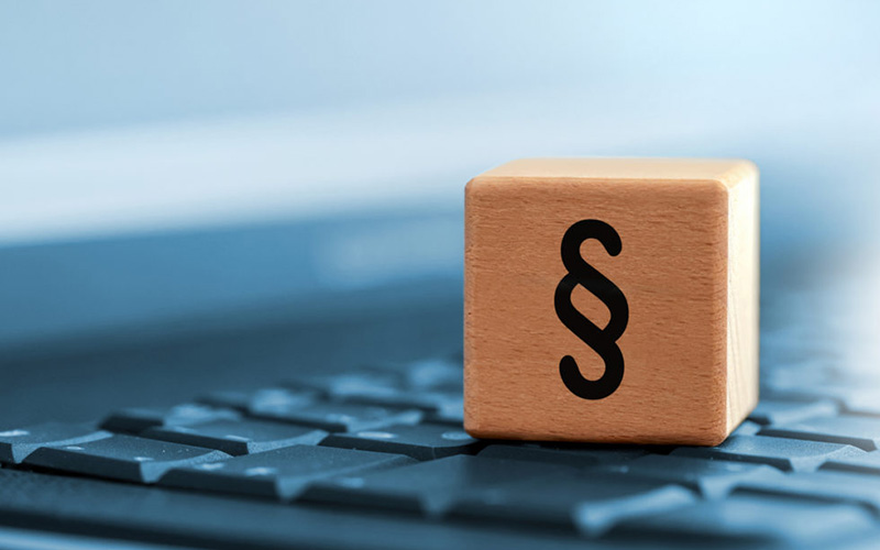 Holzwürfel mit Paragraphenzeichen steht auf einer Computertastatur, Symbol für Recht und digitale Gesetzgebung.