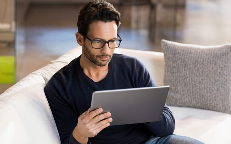 Mann sitzt mit Tablet auf dem Sofa im Home Office