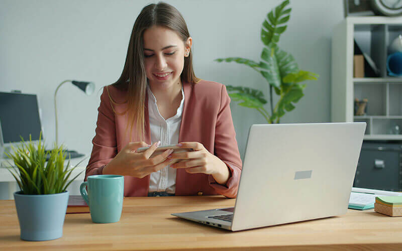 Woman sitting at her desk working on her laptop and cell phone