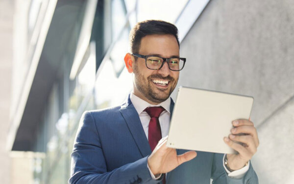 Mann mit Anzug guckt auf ein Tablet und lacht