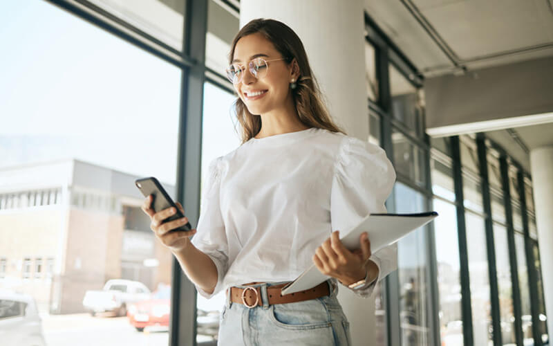 Frau hält eine Mappe in der Hand und schaut auf ihr Handy