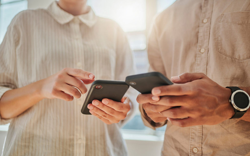 Zwei Personen stehen nebeneinander und halten beide ein Smartphone in der Hand