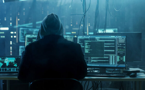 Hacker sitzt vor mehreren PCs auf denen viel Code abgebildet ist
