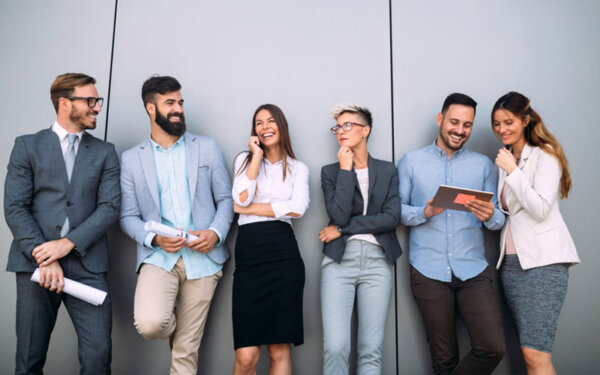 Sechs Personen im Business Kontext stehen vor einer Wand und unterhalten sich
