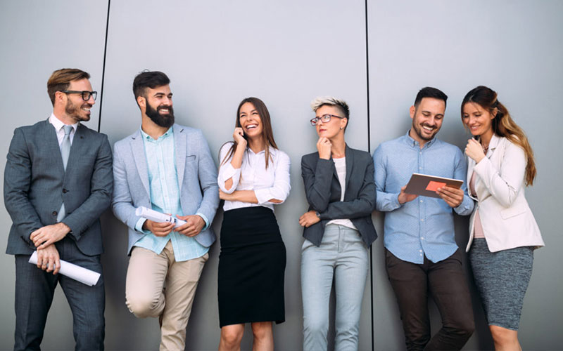 Sechs Personen im Business Kontext stehen vor einer Wand und unterhalten sich