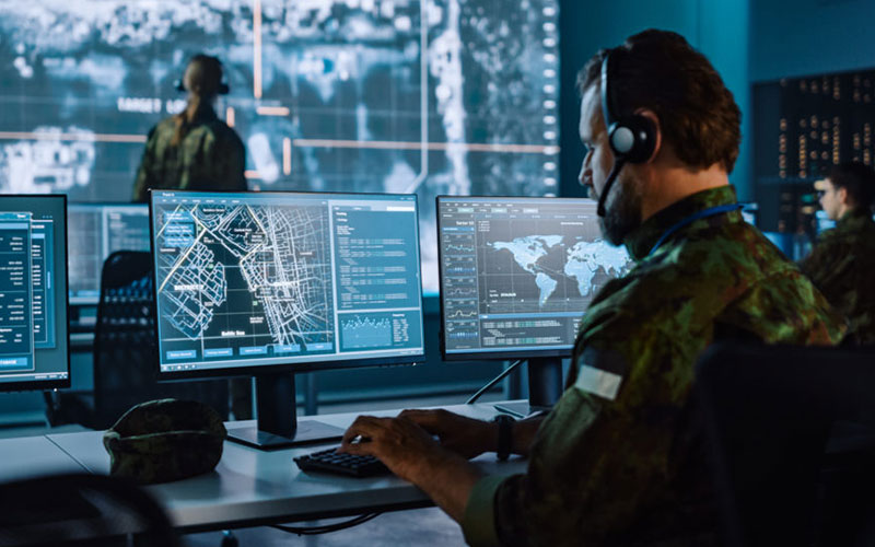 Soldat mit Headset überwacht Karten und Daten auf mehreren Monitoren
