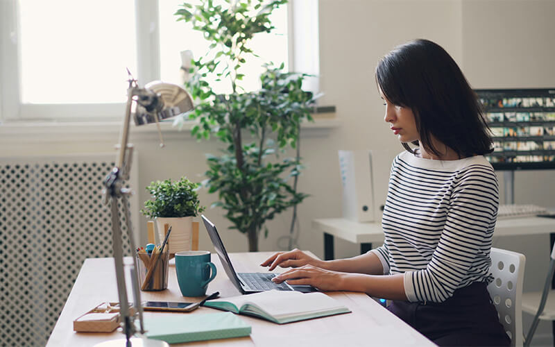 Frau sitzt am Laptop und arbeitet am Laptop im Homeoffice
