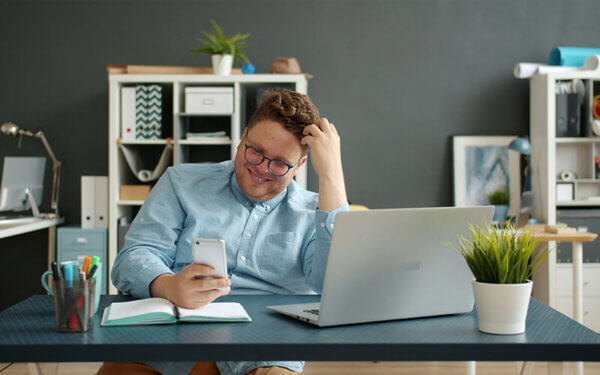 Mann sitzt an einem Schreibtisch und arbeitet am Laptop und Handy
